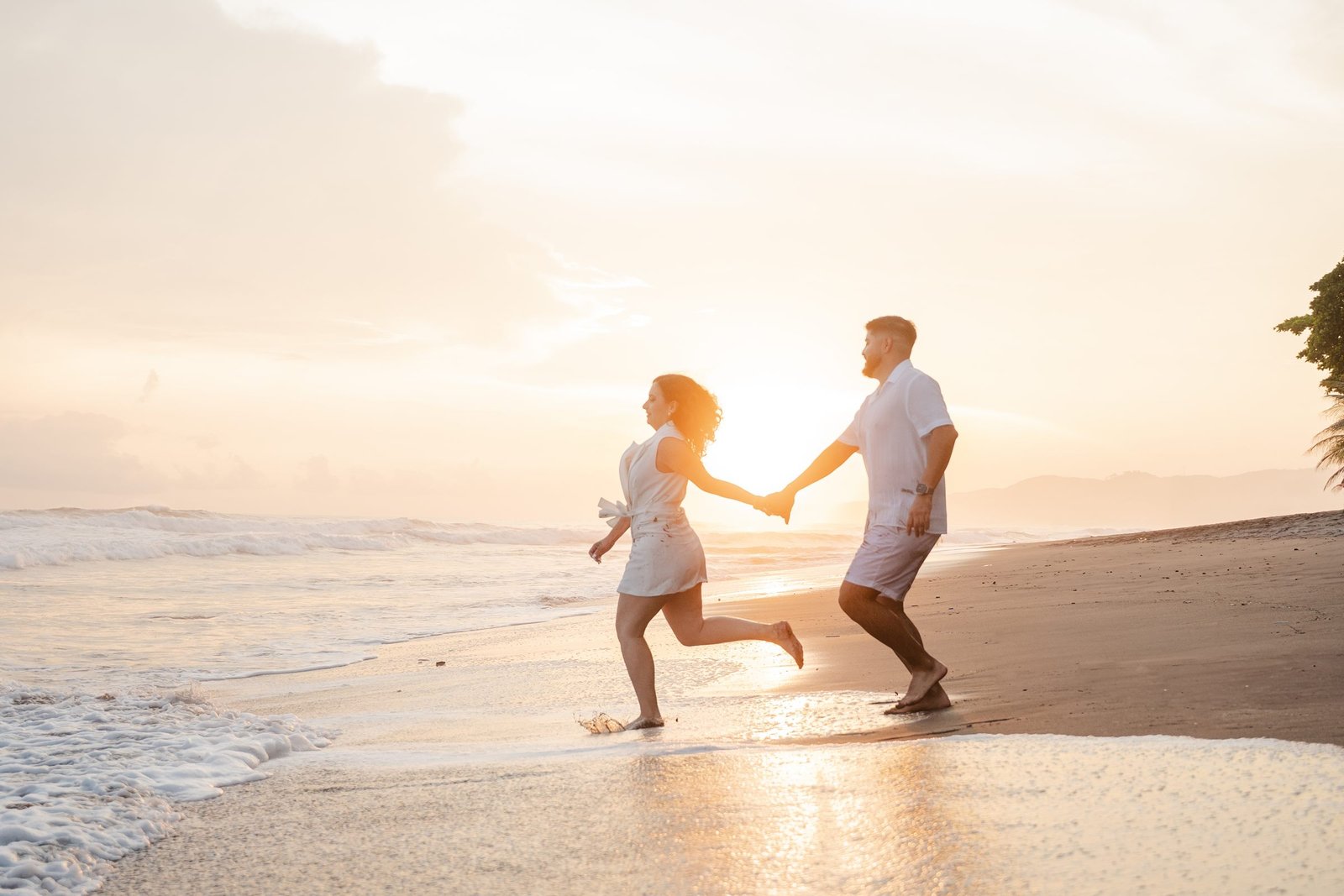 Pareja corriendo de la mano en la playa al atardecer